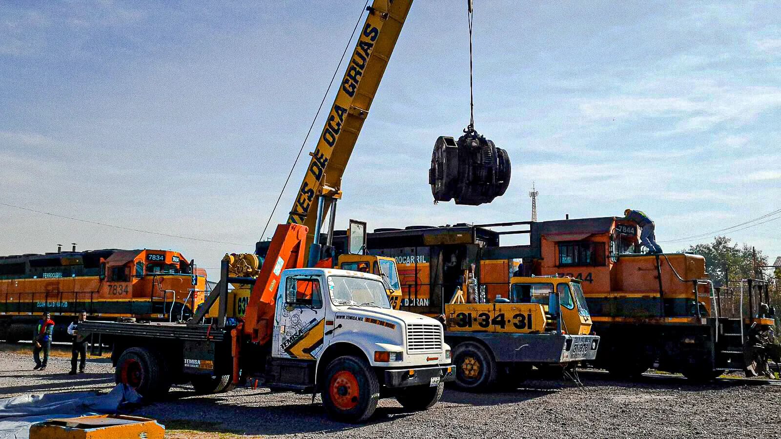 Grúa izando un motor de tracción junto a locomotoras diésel-eléctricas en un patio ferroviario, maniobra de TEMISA