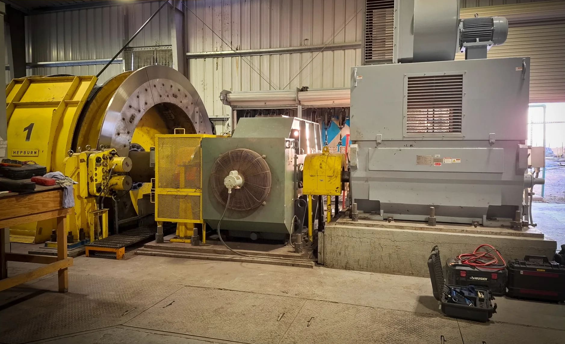 Motor eléctrico de gran potencia sobre su base de concreto en la casa de máquinas de una unidad minera, acoplado a un tambor de izaje, con maletas de herramienta de servicio en el piso