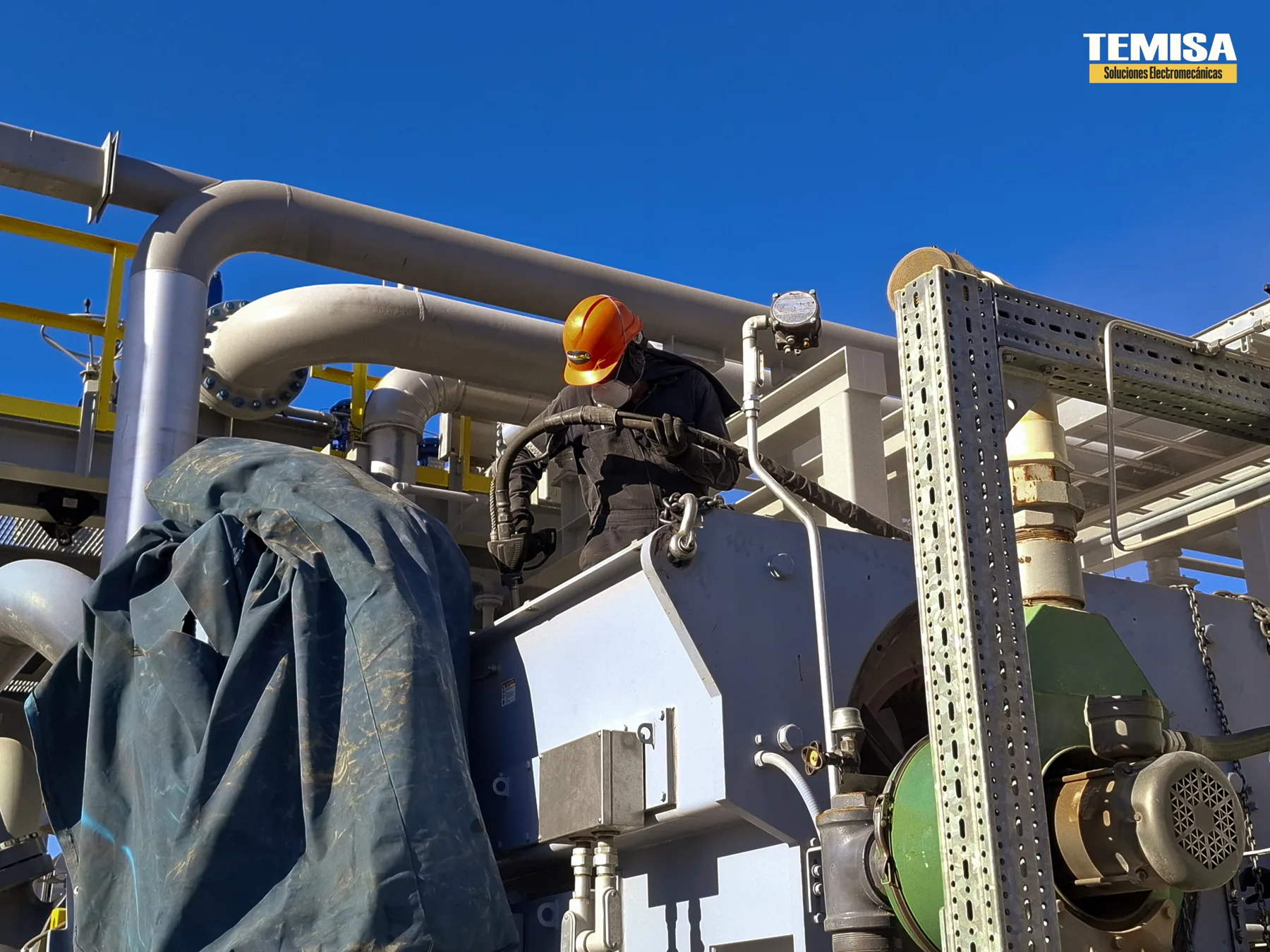 Especialista de TEMISA trabajando con manguera sobre el conjunto motor-compresor a la intemperie en una planta de proceso
