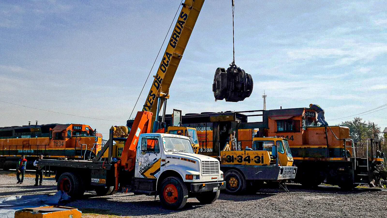 Grúa izando un motor de tracción junto a locomotoras diésel-eléctricas en un patio ferroviario, maniobra de TEMISA