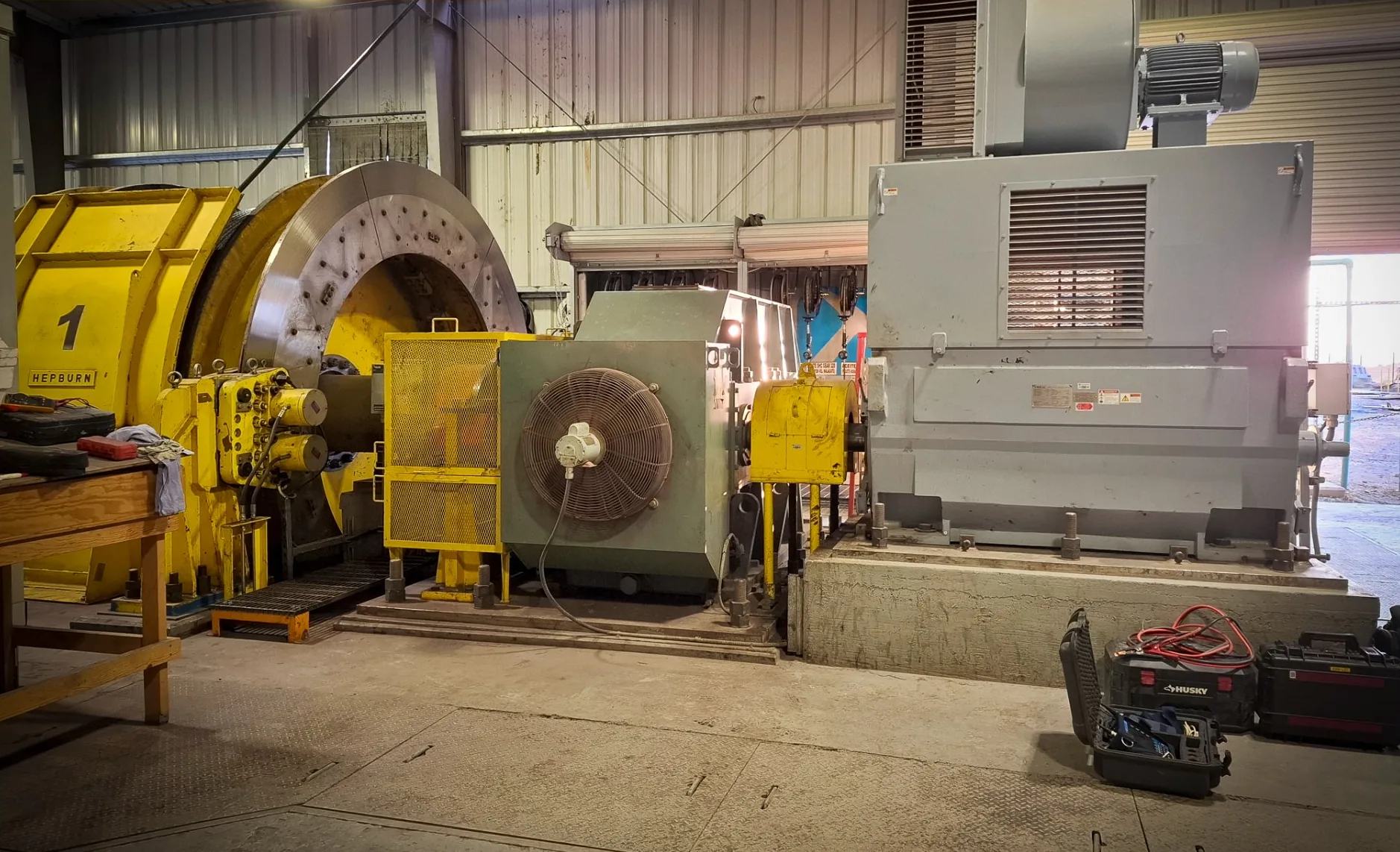 Motor eléctrico de gran potencia sobre su base de concreto en la casa de máquinas de una unidad minera, acoplado a un tambor de izaje, con maletas de herramienta de servicio en el piso